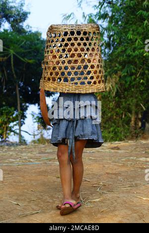 Ein junges Mädchen in einem blauen Kleid mit einem handgemachten Bambus auf dem Kopf. Ländliches Gebiet in den Bergen Thailands. Stockfoto