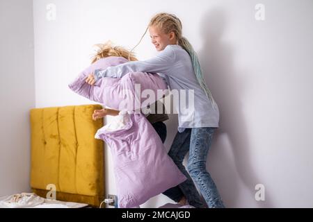 Geschwister, die Spaß haben, lachen, Junge und Mädchen spielen Kissenschlacht in einem dreckigen Kinderzimmer, Kinder spielen unter den vielen Spielzeugen zu Hause, viele Spielzeuge und Stockfoto