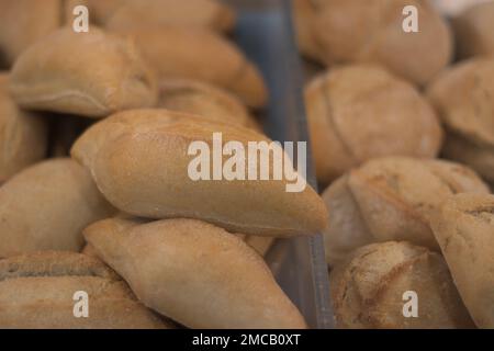 Eine Vitrine gefüllt mit kleinen Brötchen. Ein Laden mit köstlichen, knusprigen, frischen Brötchen. Frisch gebackene kleine Brötchen in einer Bäckerei. Bäckereikunst Stockfoto