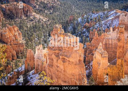 Der Bryce Canyon ist mit frisch gefallenem Schnee und fernen Bergen und leuchtend farbigen orangefarbenen Klippen geschmückt. Stockfoto