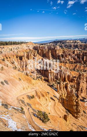 Der Bryce Canyon ist mit frisch gefallenem Schnee und fernen Bergen und leuchtend farbigen orangefarbenen Klippen geschmückt. Stockfoto