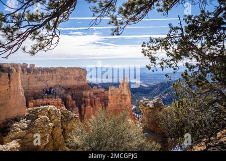 Der Bryce Canyon ist mit frisch gefallenem Schnee und fernen Bergen und leuchtend farbigen orangefarbenen Klippen geschmückt. Stockfoto