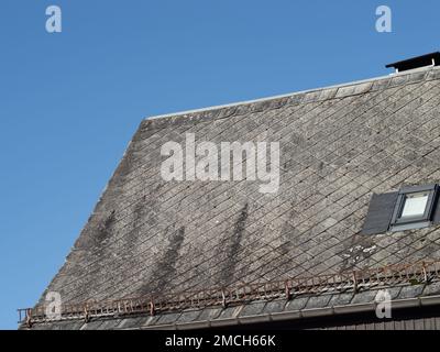 Gefährliche Asbestplatten als Dachziegel eines Wohngebäudes. Verwitterte Fassade eines Hauses. Das Material wurde in der DDR verwendet. Stockfoto