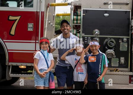 USA Air Force Airman 1. Class Janiel Elliot, 35. Civil Engineer Squadron Feuerwehrmann und junge Teilnehmer posieren vor einem Feuerwehrauto während der alljährlichen Misawa Mudder am Misawa Air Base, Japan, am 2. Juli 2022. Der Misawa Mudder wurde organisiert und unterstützt von der 35. Truppenstaffel und Outdoor Recreation. Stockfoto