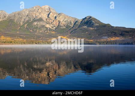 Pyramid Mountain mit Blick auf den Pyramid Lake mit einer Schicht Morgennebel an der Wasseroberfläche an einem sonnigen Tag. Jasper National Park, Alberta, Kanada Stockfoto