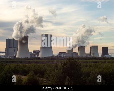 Rauch eines Braunkohlekraftwerks. Treibhausgase, die die Luft in einem ländlichen Gebiet verschmutzen. Kühltürme mit Schornsteinen in der Landschaft. Stockfoto