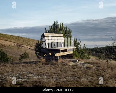 Leere Parkbank auf einem Hügel in der Natur. Die ruhige und idyllische Landschaft liegt im Hintergrund. Schöner Ort zum Ausruhen in einer ländlichen Gegend. Stockfoto