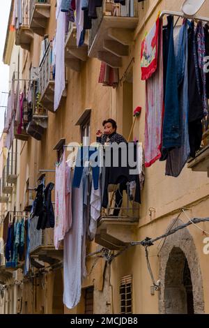 Enge Gasse in Trapani mit Balkonen, hängender Wäsche und einer Frau, die auf dem Balkon raucht. Stockfoto