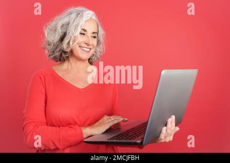 Eine lächelnde, reife Frau, die steht und ein Notebook benutzt Stockfoto