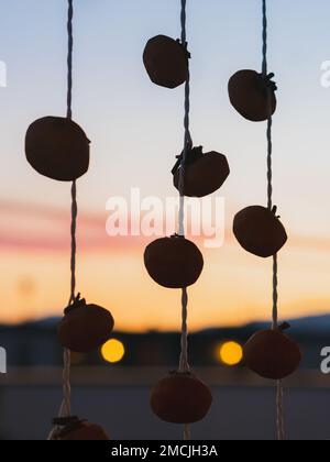 Silhouette-Blick auf hängende Persimone - Japanische getrocknete Persimone (Hoshigaki), die an Streicher gehängt wurden, um einen gewöhnlichen Anblick in Yamagata während des Sonnenuntergangs zu trocknen. Stockfoto