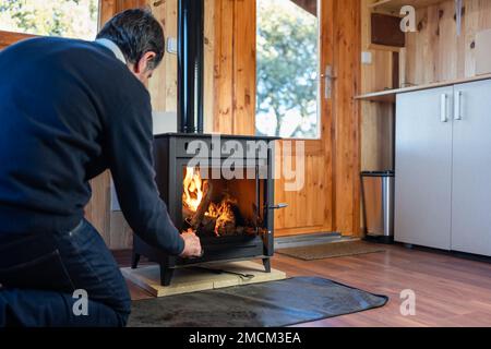 Mann, der das Feuer in einem rustikalen gusseisernen Kamin schürt, um das Haus im Winter zu heizen Stockfoto
