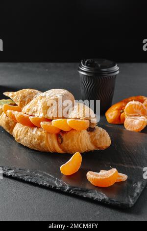 Croissant mit süßen Mandarinen auf dunklem Hintergrund. Hausgemachte Croissants Stockfoto