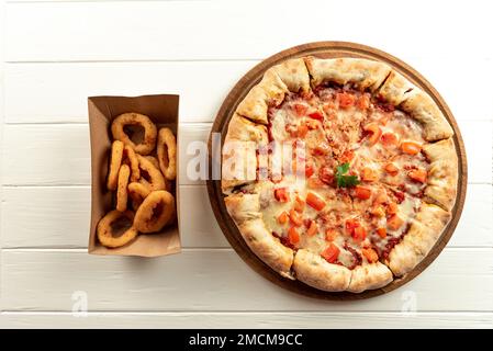 Lieferkonzept. Neapalitanische Pizza mit Tomaten auf Weiß mit Vorspeisen. Pizza und Vorspeisen nebeneinander auf weißem Dach Stockfoto