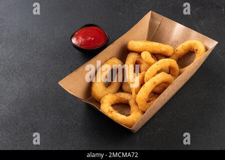 Tintenfischringe in einer Papierkiste auf dunklem Hintergrund. Konzept der Lieferung nach Hause Stockfoto