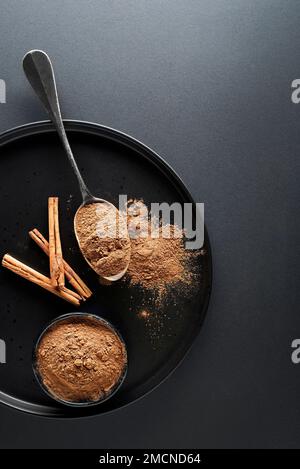 Aromatische Zimtstangen und Tasse mit Zimtpulver auf schwarzem Hintergrund Stockfoto