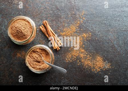 Gemahlener Zimt in Glasbechern und Zimtstangen mit Pulver auf grauem rustikalem Hintergrund Stockfoto