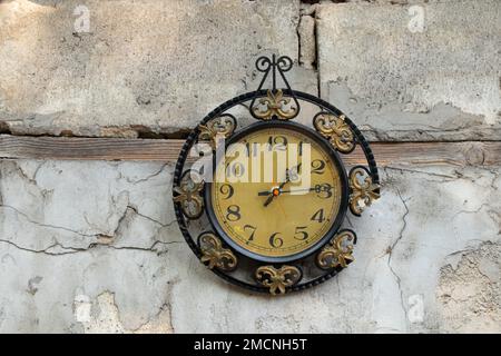 Alte kaputte Uhr udssr hängt an der weißen Wand eines Hauses in der Straße in der Sonne, gebrochene alte Wanduhr Stockfoto