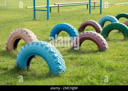 Alte, mit Farbe lackierte Reifen werden auf dem Kinderspielplatz zum Anbringen auf dem Boden vergraben, die Reifen auf dem Rasen Stockfoto