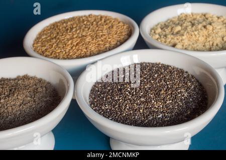 Nahaufnahme einer Schüssel mit Chiasamen zusammen mit kleinen Gerichten mit ganzen und pulverförmigen Chiasamen und Leinsamen. Essen und gesunde Ernährung. Stockfoto