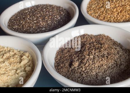 Nahaufnahme einer Schüssel mit Chiasamen-Pulver zusammen mit anderen Schüsseln voller und pulverisierter Chiasamen und Leinsamen. Essen und gesunde Ernährung. Stockfoto