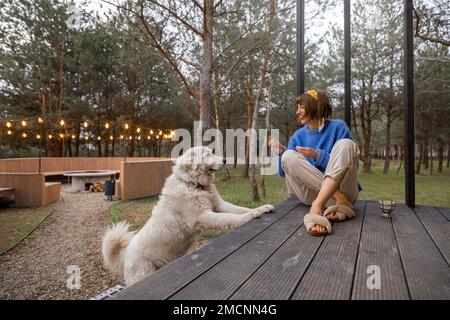 Eine Frau mit Hund ruht in der Nähe einer hölzernen Hütte in der Natur Stockfoto