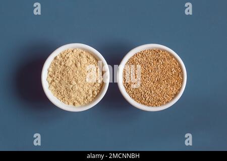 Draufsicht einer Nahaufnahme zweier Keramikschüsseln nebeneinander mit ganzen und pulverförmigen Flachssamen. Superfood. Stockfoto