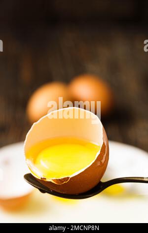 Halbgeschnittenes rohes Ei auf Löffel, Eigelb sichtbar, goldgelb, umgeben von Eiweiß, Löffel als Utensilien. Stockfoto