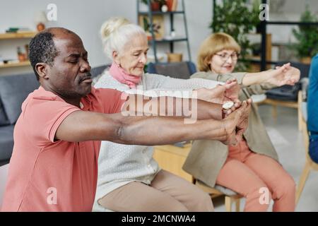 Gruppe von Senioren, die gemeinsam Morgenübungen im Raum machen Stockfoto