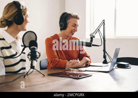 Fröhliche Podcaster, die eine gute Zeit haben, während sie eine Audioübertragung in einem Heimstudio moderieren. Lächelnde Content-Ersteller, die einen Internet-Podcast aufzeichnen Stockfoto