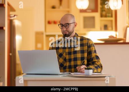 Porträt eines jungen Weißen mit Brille, der am Laptop arbeitet. Arbeiter, der Computer verwendet. Konzept von Fernarbeit und Freiberufler. Stockfoto
