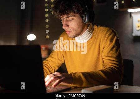 Junger arabischer Geschäftsmann oder Student, der per Fernzugriff Überstunden macht, zu Hause oder in dunklen Schlafzimmern mit einem Laptop-Computer online lernt Stockfoto
