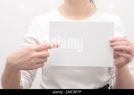 Eine Frau hält ein leeres weißes Blatt Papier und zeigt mit dem Zeigefinger. Stockfoto