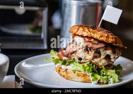 Köstliches gegrilltes Rindfleisch und Schinkenburger mit Salat und Mayonnaise auf einem Holztisch in einem Café, mit Kopierbereich Stockfoto