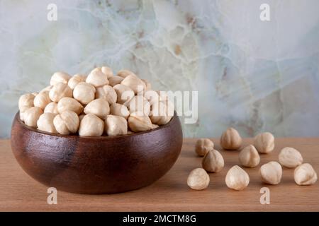 Schüssel voll mit geschälten Haselnüssen auf einem Holztisch, Vorderansicht Stockfoto