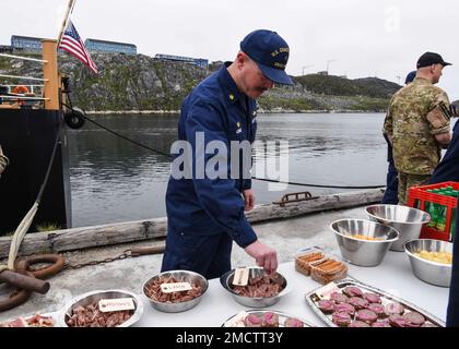 UCGC Oak (WLB 211) Befehlshaber LT. Commander. Jacob Loman probiert geräucherte Rentiere während einer Begrüßungsveranstaltung in Nuuk, Grönland, am 9. Juli 2022. USA Mitglieder der Küstenwache und aus Frankreich, Dänemark und Grönland trafen sich zu einem moralischen Ereignis am Ende der fünftägigen Übung Argus. USA Foto der Küstenwache von Petty Officer 2. Klasse Diana Sherbs. Stockfoto