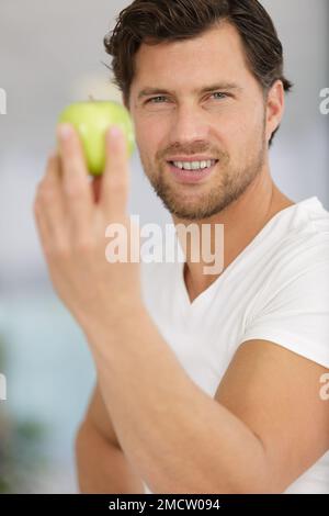Ein Mann mittleren Alters, der gesunden grünen Apfel mit einem glücklichen Gesicht isst Stockfoto