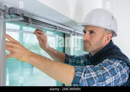 Bauarbeiter, der im Haus ein Schaumstoffband auf das Fenster legt Stockfoto