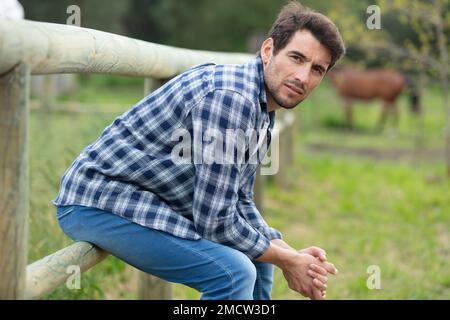 Ein Mann ruht auf einem Zaun auf einer Pferdefarm Stockfoto