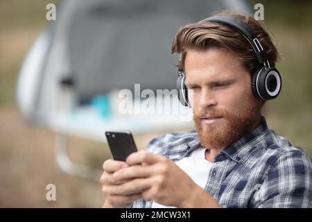 Junger Mann, der vor dem Zelt sitzt und Musik hört Stockfoto