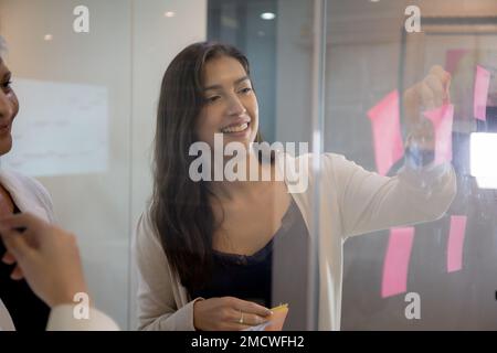 Gruppe von Team-Business-Mitarbeitern, die sich mit Haftnotizen über das Marketing im Büro, die Idee und das auf Glas stellen, Brainstorming und Meetings für die Planung durchführen Stockfoto