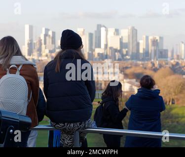 Menschen, die auf Geländern auf dem Hügel im Greenwich Park sitzen und die Aussicht auf Canary Wharf bewundern. London, England Stockfoto