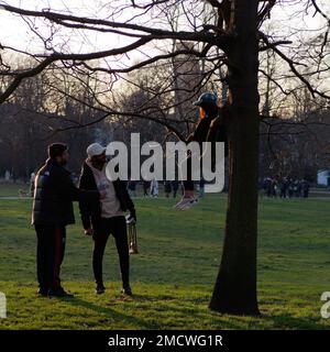 Frauen sitzen auf einem Baum im Greenwich Park, während sie sich mit zwei Freunden unterhält. London, England Stockfoto