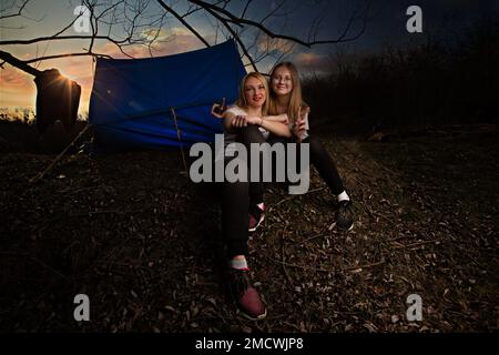 Die Familie, Mutter und Tochter, gingen übers Wochenende auf die Landschaft für ein Picknick, saßen am Feuer in freier Wildbahn mit einem Zelt, braten Kartoffeln, trinken heißen Tee. Hochwertiges Foto Stockfoto