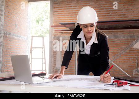 Junge, weiße Architektin, die auf einem Laptop sitzt und einen Entwurf für die Planung eines Gebäudes auf dem Schreibtisch zeichnet, Ingenieur denkt und skizziert blau Stockfoto