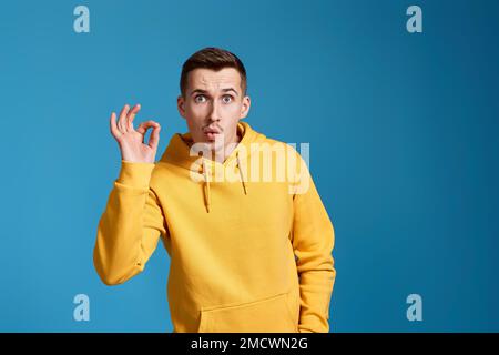 Junger Mann in gelbem Sweatshirt, der eine gute Geste zeigt Stockfoto