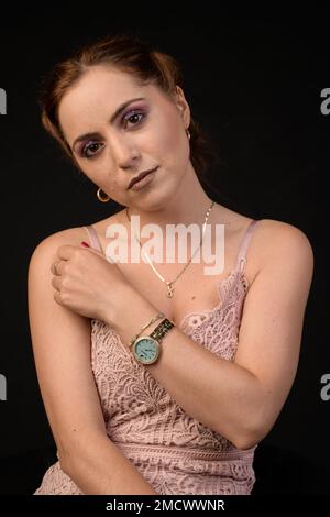 Hübsche junge Frau mit geschminkten Augen in ärmellosem rosa Kleid auf schwarzem Hintergrund Stockfoto