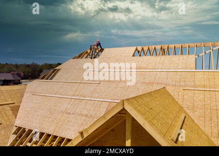 Ein unvollendetes Haus wird von einem Dachdecker neu bedeckt, der an der Installation eines Sperrholzdachs arbeitet Stockfoto