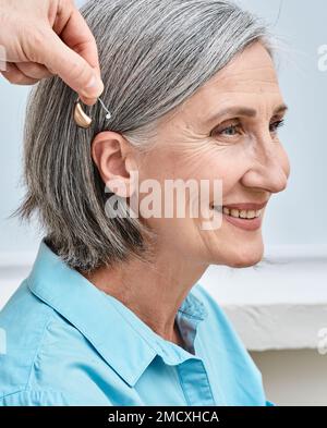 Arzt-Audiologe, der Hörgeräte am Ohr einer Seniorin anwendet. Hörgeschädigte Frau braucht Hörgeräte Stockfoto