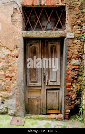 Vintage-Doppeltür aus Holz in einer roten gemauerten Backsteinwand mit einem großen Grill darüber, Roccatederighi Mountain Village, Toskana, Italien, Stockfoto