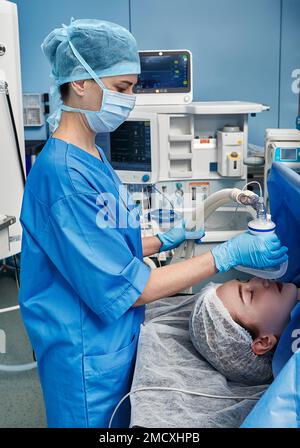Chirurgische Krankenschwester in sterilen Handschuhen Anästhesiemaske auf Patientin legen während der Operation im Krankenhausoperationssaal Stockfoto
